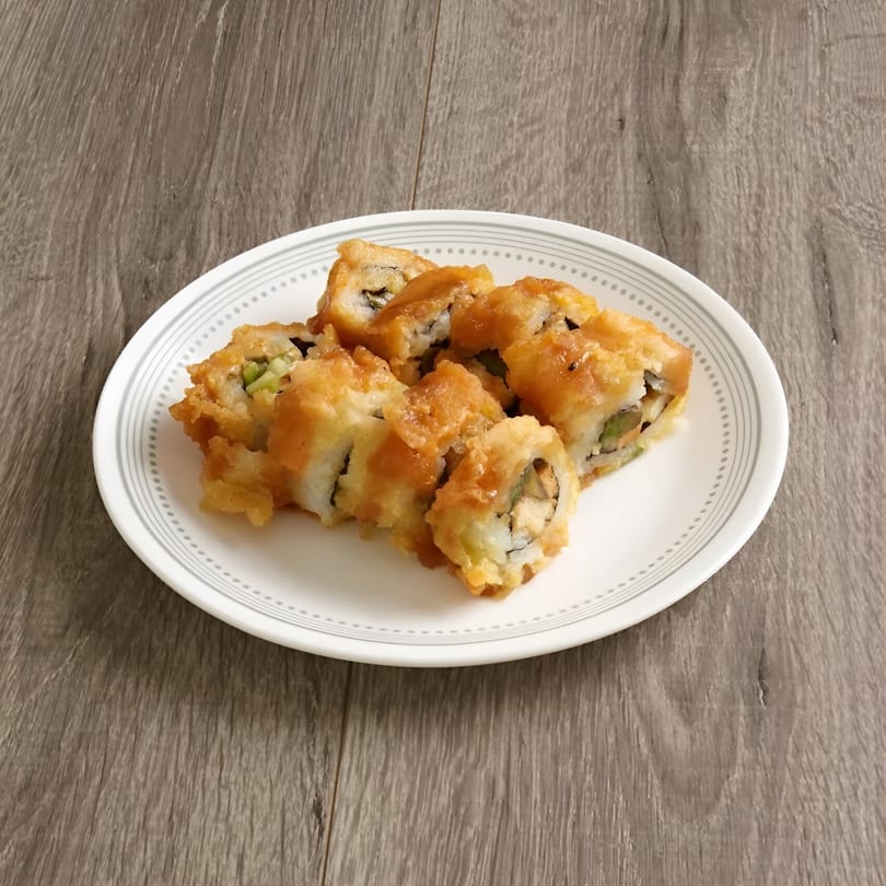 A white plate holds several pieces of golden-fried vegetarian sushi rolls on a wooden table.
