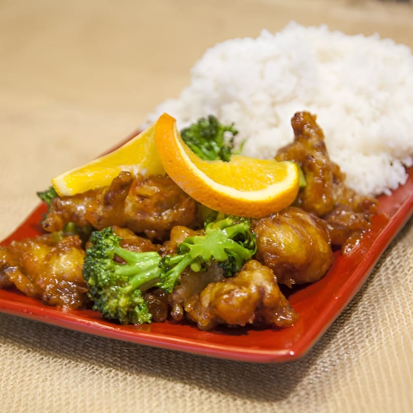 Veggie House's orange "chicken" with broccoli, rice, and orange slices on a red plate.